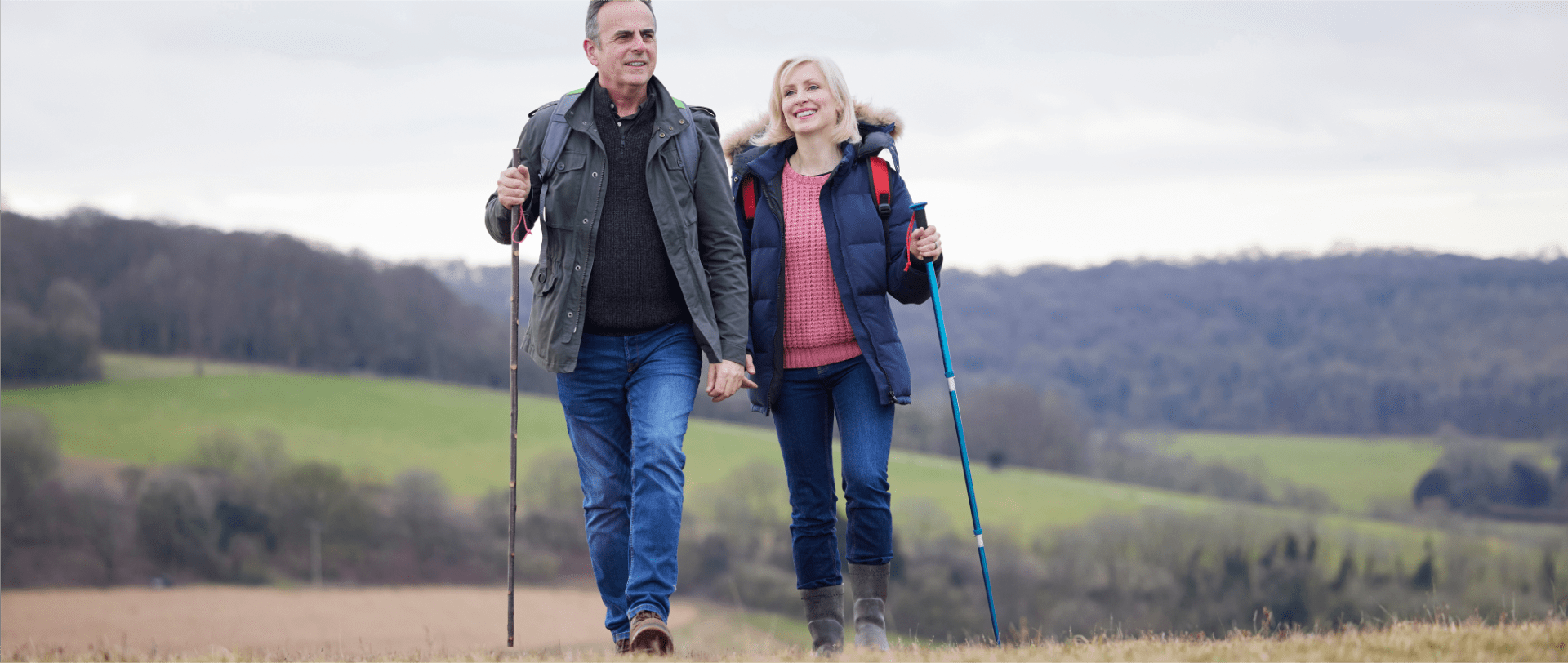 A happy couple enjoying a scenic walk in the countryside, both wearing comfortable shoes that support their bunions. The couple smiles and holds hands as they take in the beautiful surroundings, enjoying the freedom and relaxation of a day outdoors.