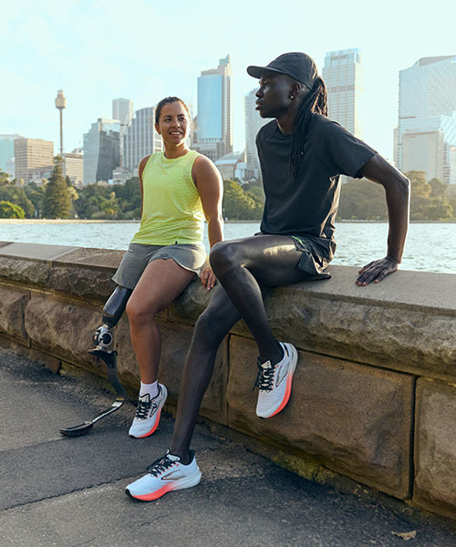 A man and a woman sitting on the edge of a bridge, wearing Brooks trainers.